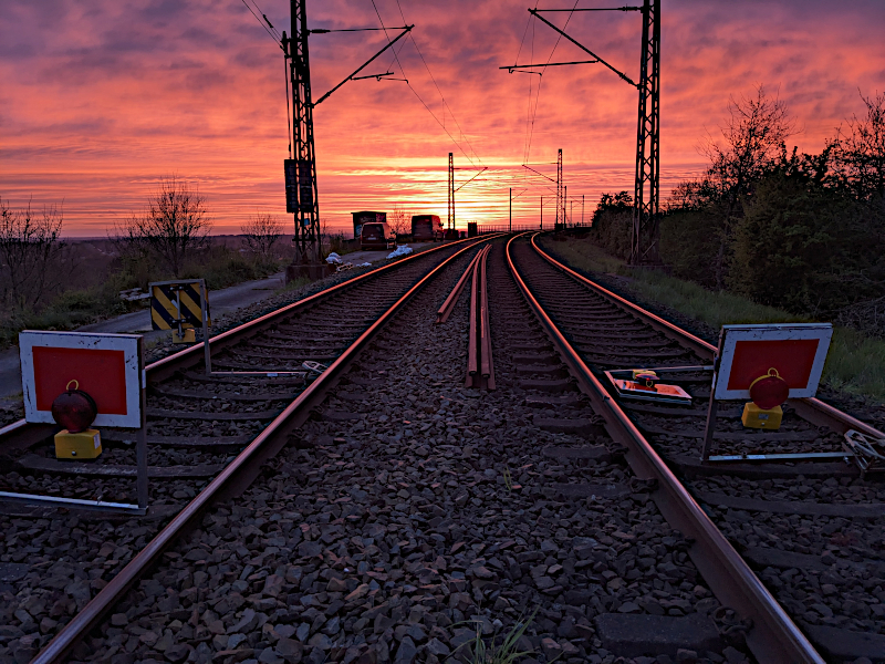 Im Vordergrund die Schienen derRendsburger Hochbrücke, die auf eine im Abendrot leuchtende Wasserfläche und den darüberliegenden, leicht bewölkten Himmel zulaufen