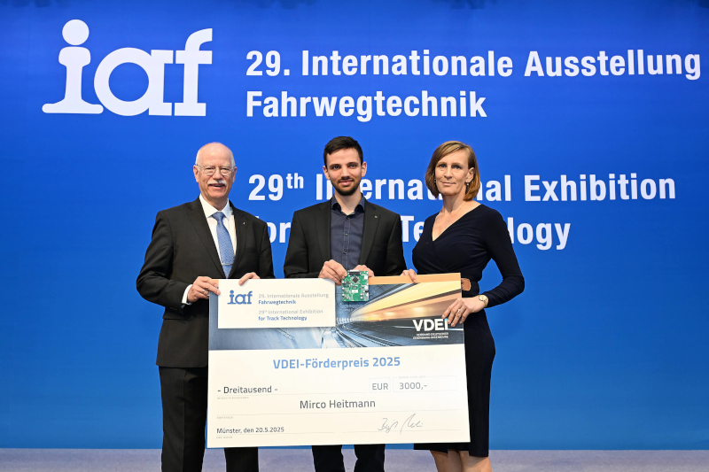 Ein Foto von dem Preisträger mit zwei Vertretern des VDEI-Präsidiums; zu dritt halten Sie einen symbolischen Scheck mit dem Preisgeld; im Hintergrund das Logo der Messe iaf