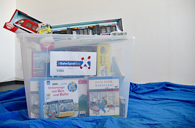 Eine durchsichtige Box aus Kunststoff, die Spiele und Bücher zum Thema Bahn enthält